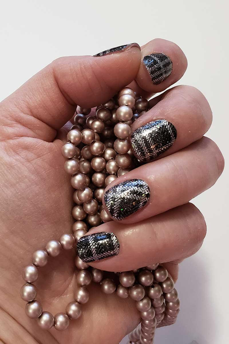 Black plaid glitter manicured hand holding bronze pearls